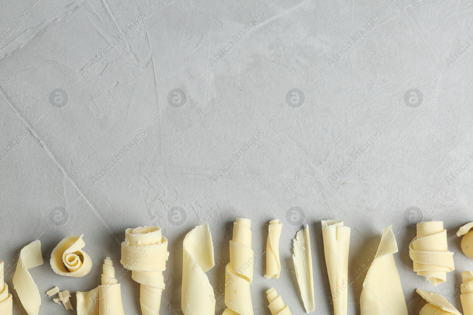 Photo of White chocolate curls and space for text on gray background, top view