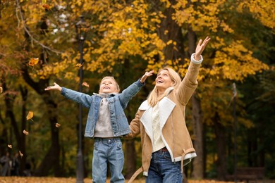 Photo of Happy mother and her son playing with dry leaves in autumn park