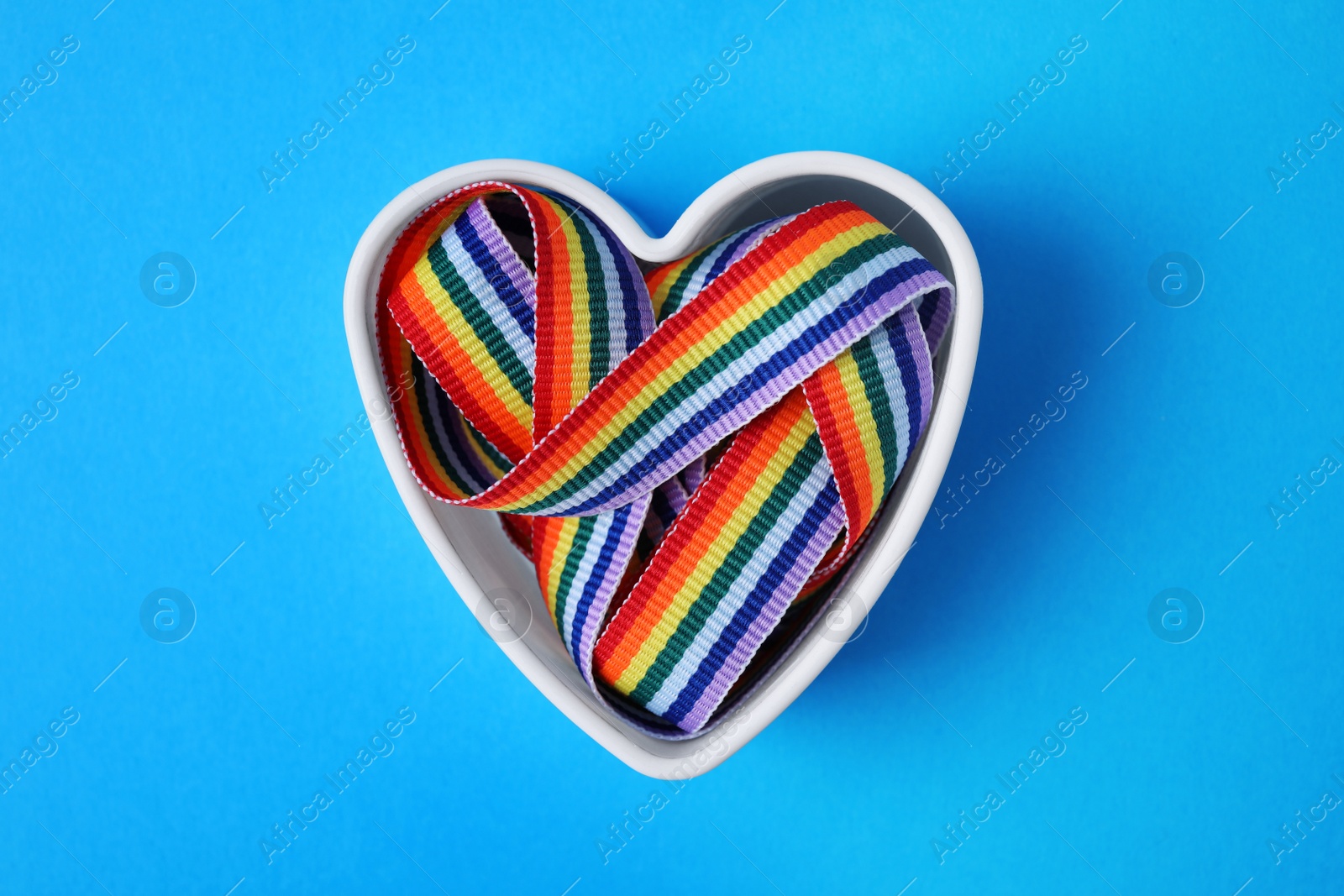 Photo of Heart shaped mold with bright rainbow ribbon on color background, top view. Symbol of gay community