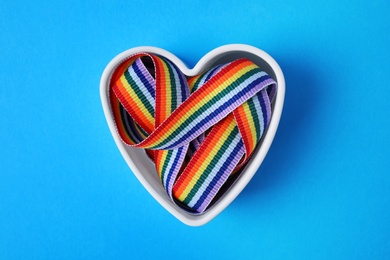 Heart shaped mold with bright rainbow ribbon on color background, top view. Symbol of gay community