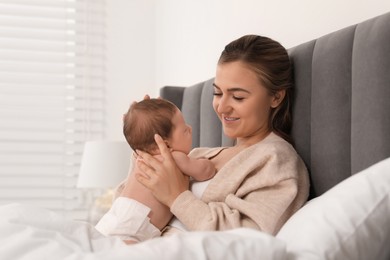 Mother holding her cute newborn baby in bed indoors, space for text