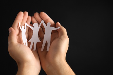 Photo of Man holding paper silhouette of family in hands on black background, closeup. Space for text