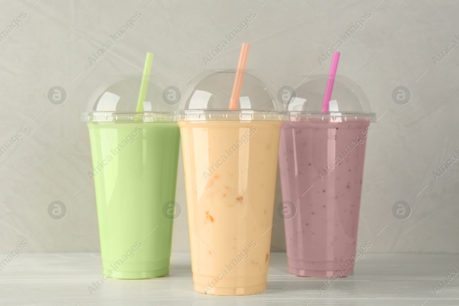 Photo of Plastic cups of different tasty smoothie on white wooden table