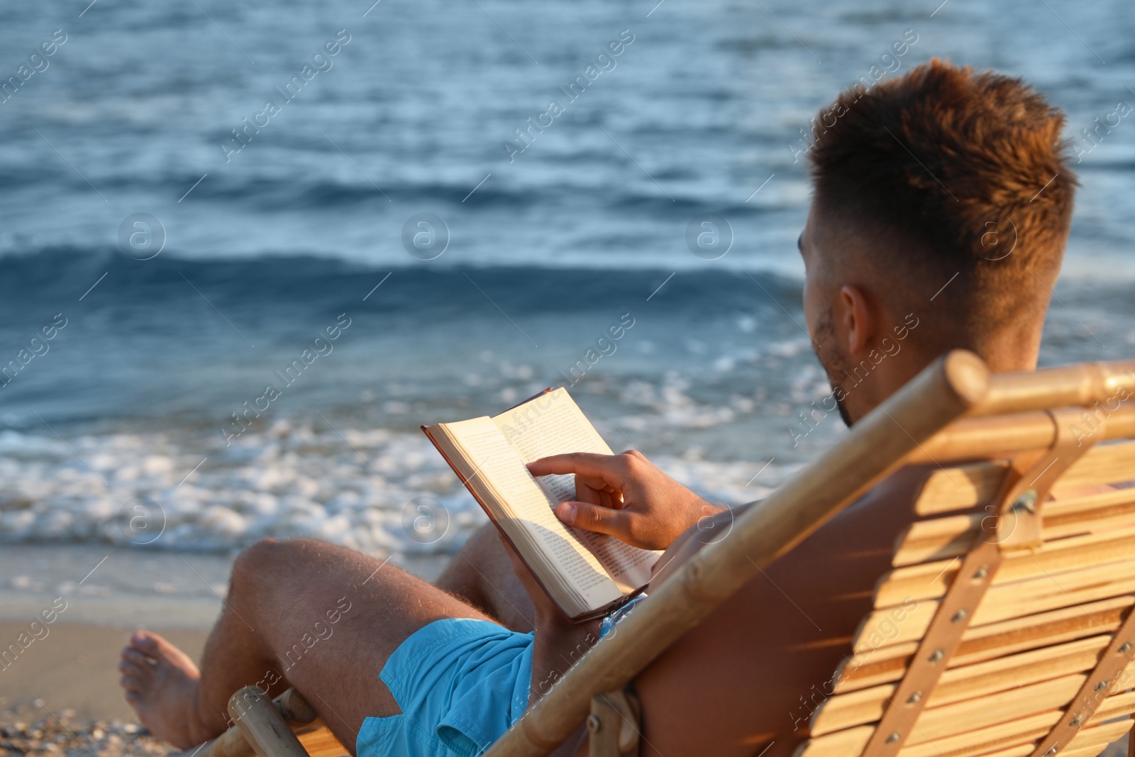 Photo of Young man reading book on sandy beach near sea