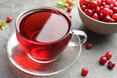 Photo of Tasty hot cranberry tea in glass cup and fresh berries on light grey textured table