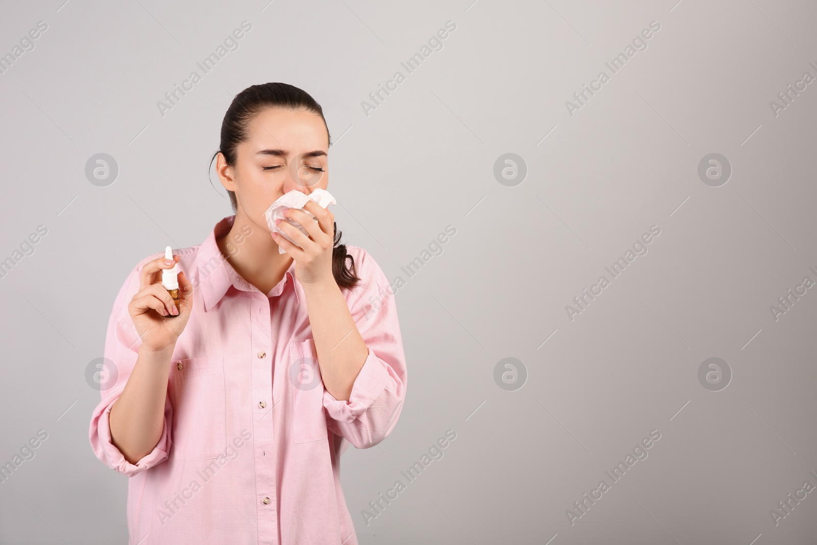 Photo of Woman with nasal spray and tissues on light grey background, space for text