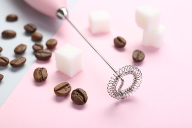 Pink milk frother wand, coffee beans and sugar cubes on color background, closeup