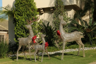 Photo of Funny reindeers with red bows near house. Festive outdoor Christmas decoration