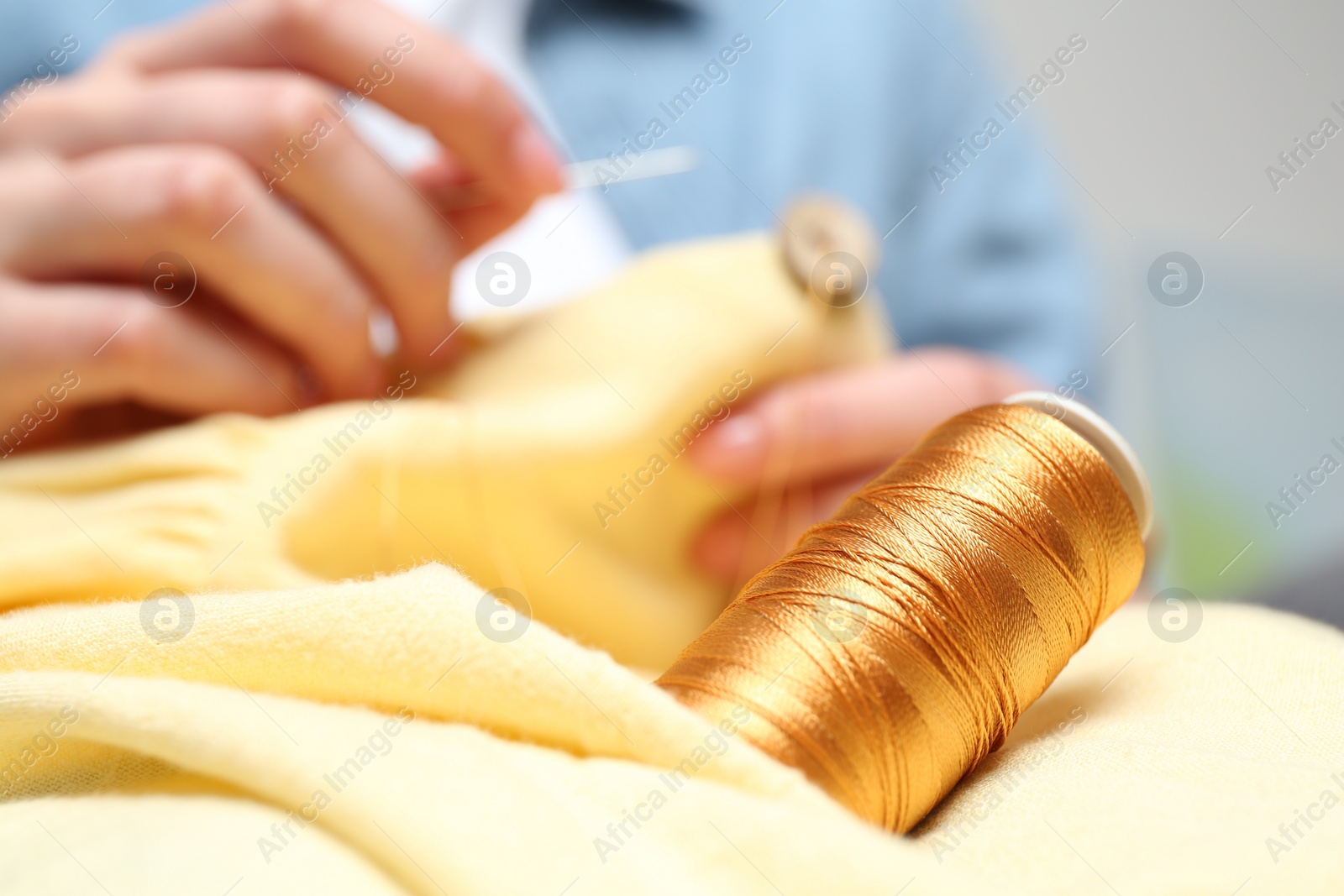 Photo of Woman sewing button onto shirt, focus on thread spool