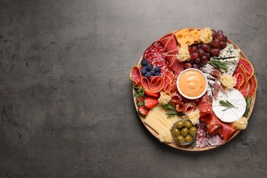 Photo of Wooden plate with different delicious snacks on grey table, top view. Space for text