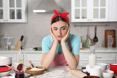 Photo of Upset housewife at messy countertop in kitchen. Many dirty dishware, food leftovers and utensils on table