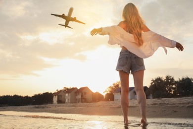 Image of Woman on beach looking at airplane flying in sky, back view