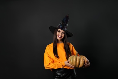 Photo of Beautiful woman wearing witch costume with pumpkin for Halloween party on black background