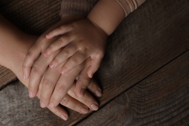 Family holding hands together at wooden table, top view. Space for text