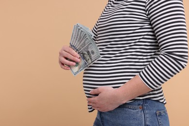 Surrogate mother. Pregnant woman with dollar banknotes on beige background, closeup. Space for text