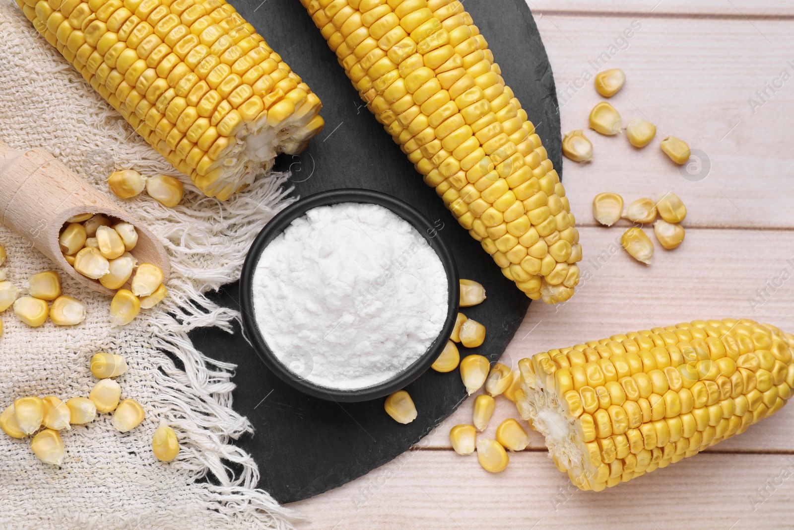 Photo of Bowl with corn starch, ripe cobs and kernels on wooden table, flat lay