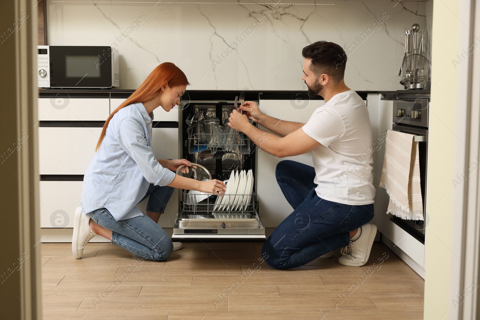 Photo of Lovely couple loading dishwasher with plates in kitchen