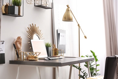 Photo of Modern workplace with laptop and golden decor on desk near wall. Stylish interior design