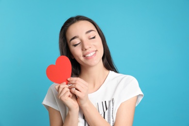 Photo of Portrait of beautiful young woman with paper heart on color background