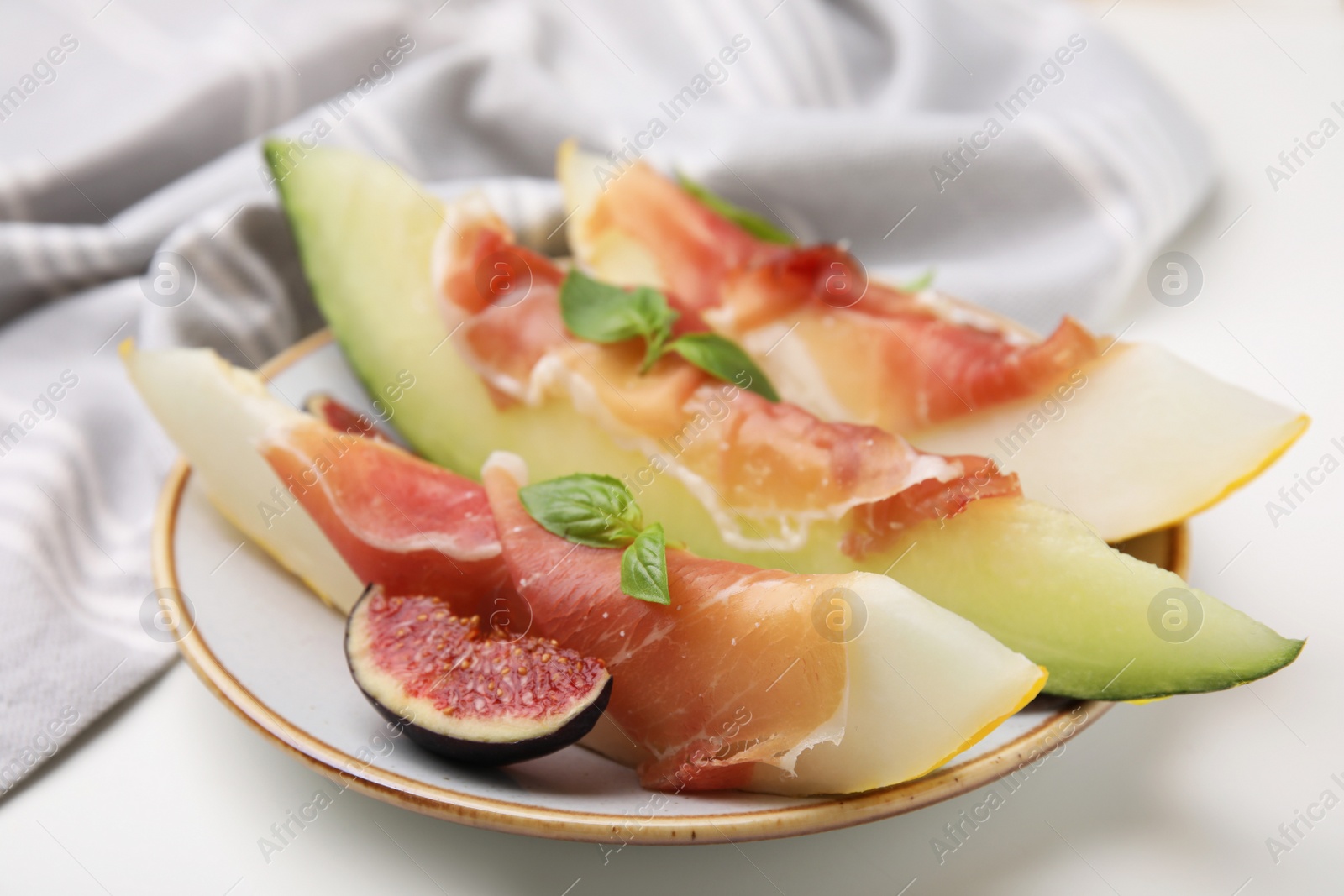 Photo of Plate of tasty melon, jamon, and figs on white table, closeup