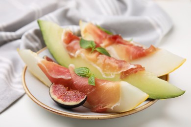 Plate of tasty melon, jamon, and figs on white table, closeup