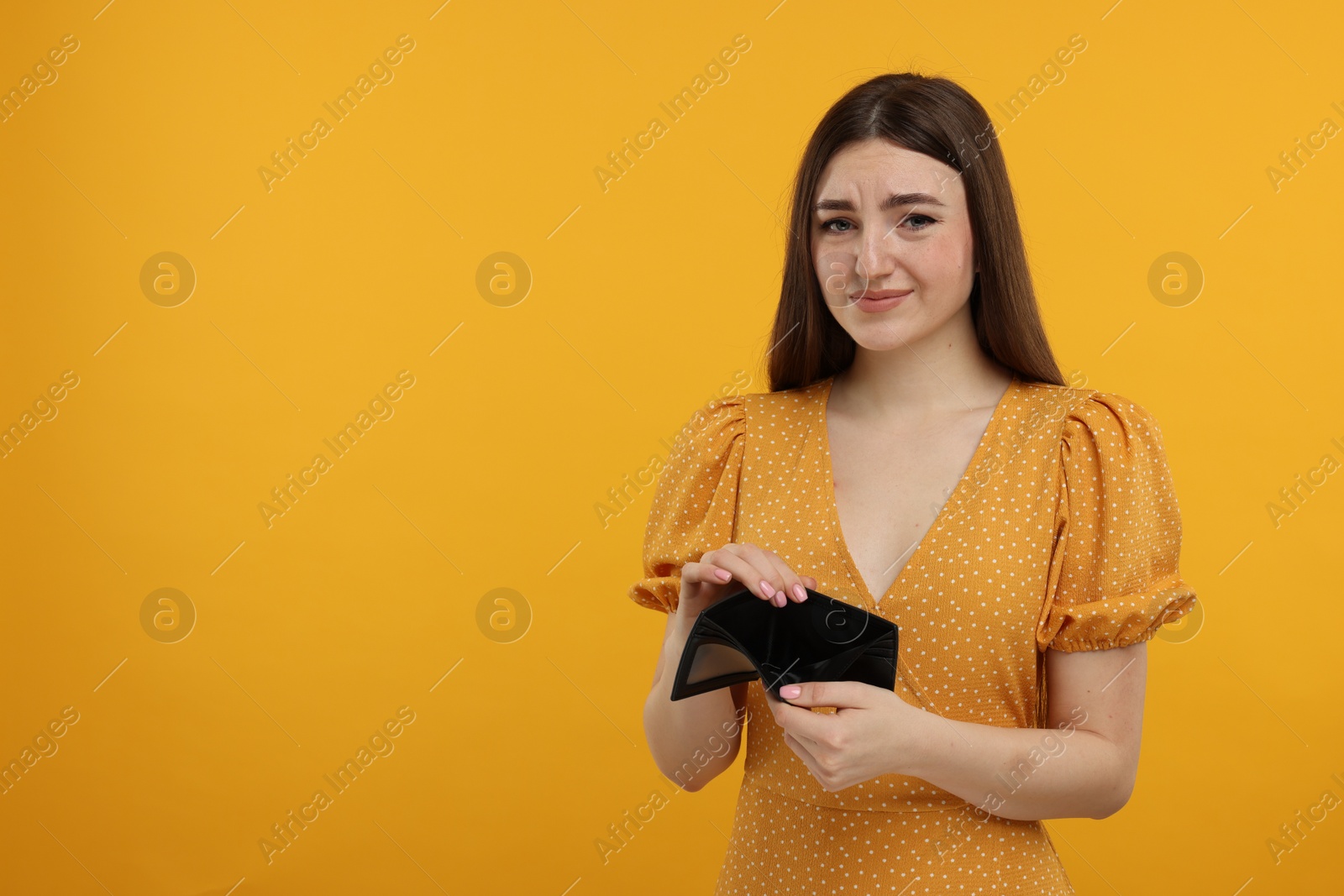 Photo of Sad woman showing empty wallet on orange background, space for text