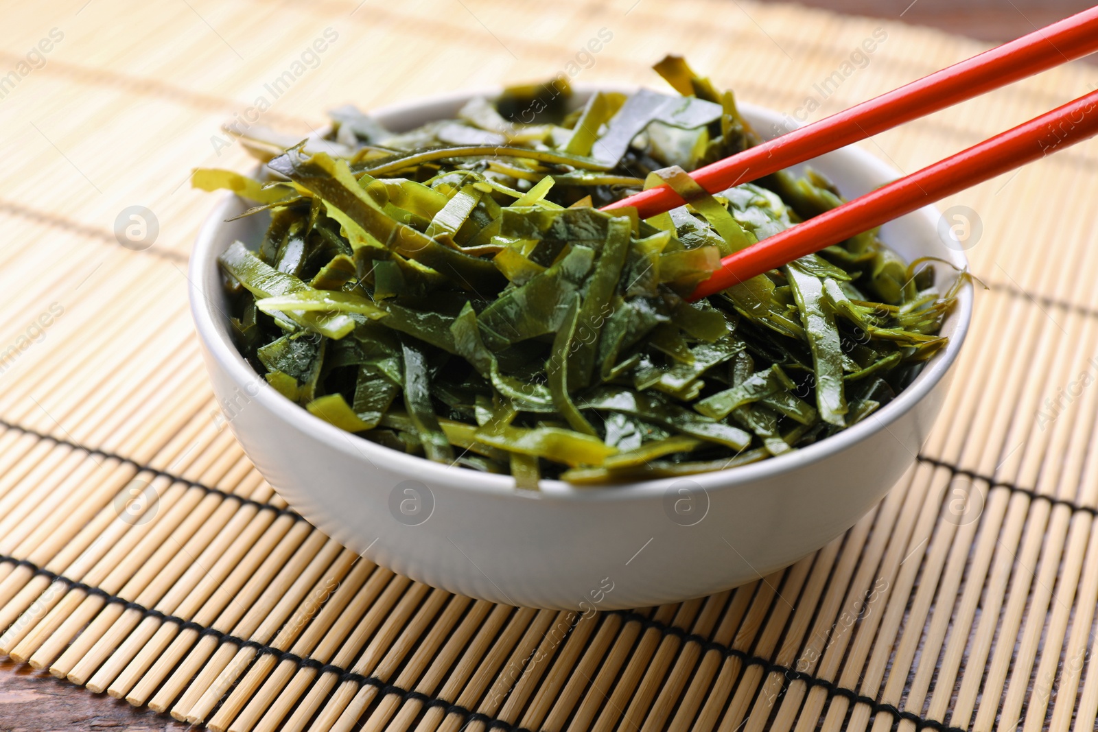 Photo of Fresh laminaria (kelp) seaweed in bowl and chopsticks on table, closeup