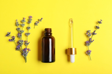 Photo of Bottle of essential oil and lavender flowers on yellow background, flat lay
