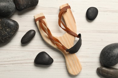 Photo of Slingshot with stones on white wooden table, flat lay