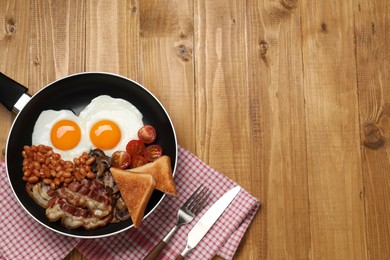 Photo of Frying pan with cooked traditional English breakfast on wooden table, flat lay. Space for text