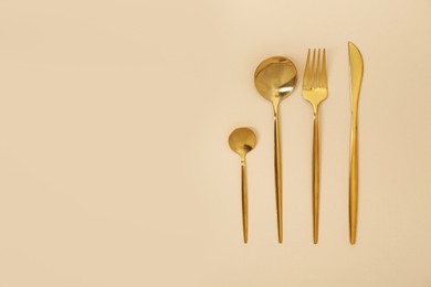 Photo of Stylish golden cutlery set on beige background, flat lay. Space for text