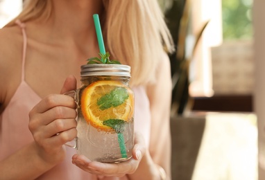 Photo of Young woman with mason jar of tasty natural lemonade in cafe, closeup. Detox drink