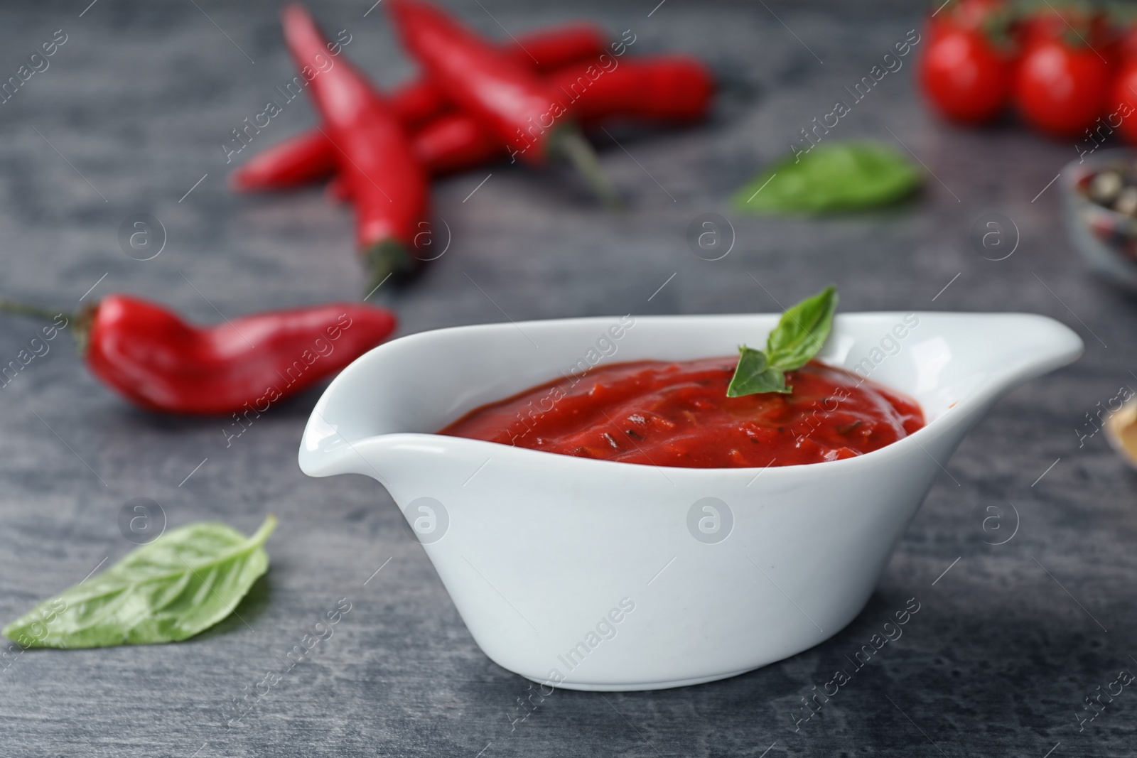 Photo of Gravy boat with spicy chili sauce on dark table