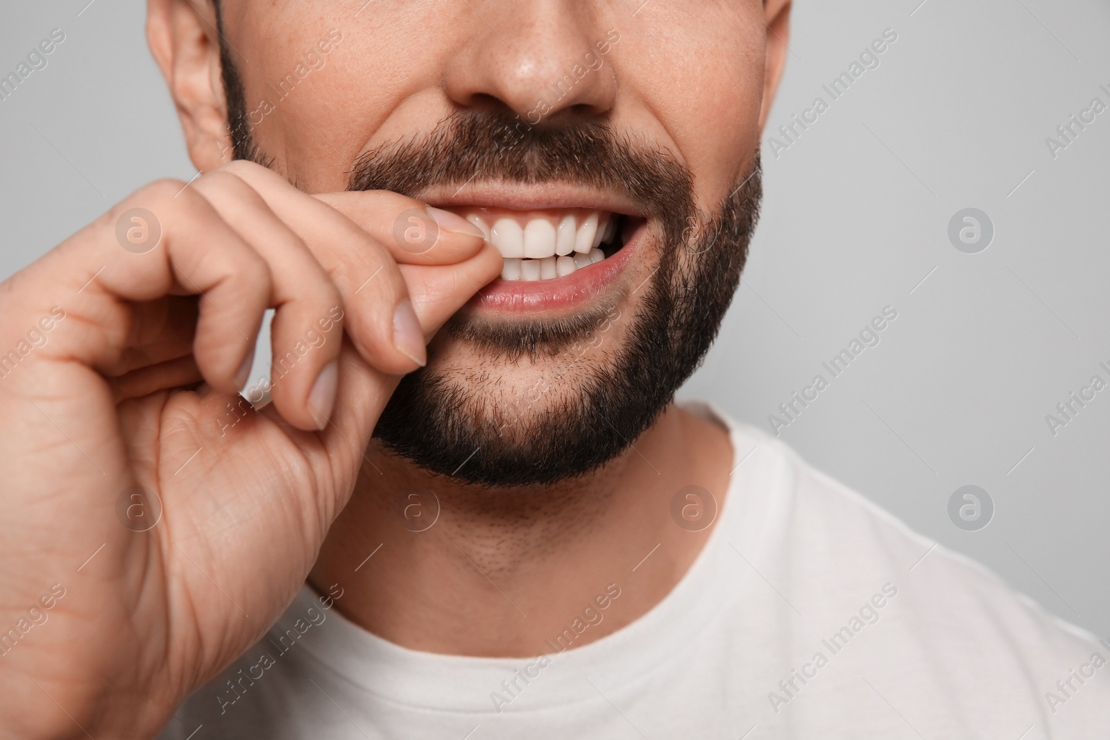 Photo of Man biting his nails on grey background, closeup