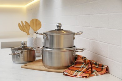 Photo of Set of stainless steel cookware and kitchen utensils on table near white brick wall