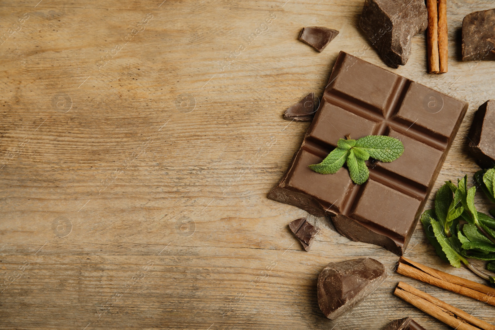 Photo of Tasty chocolate pieces, cinnamon sticks and mint on wooden table, flat lay. Space for text