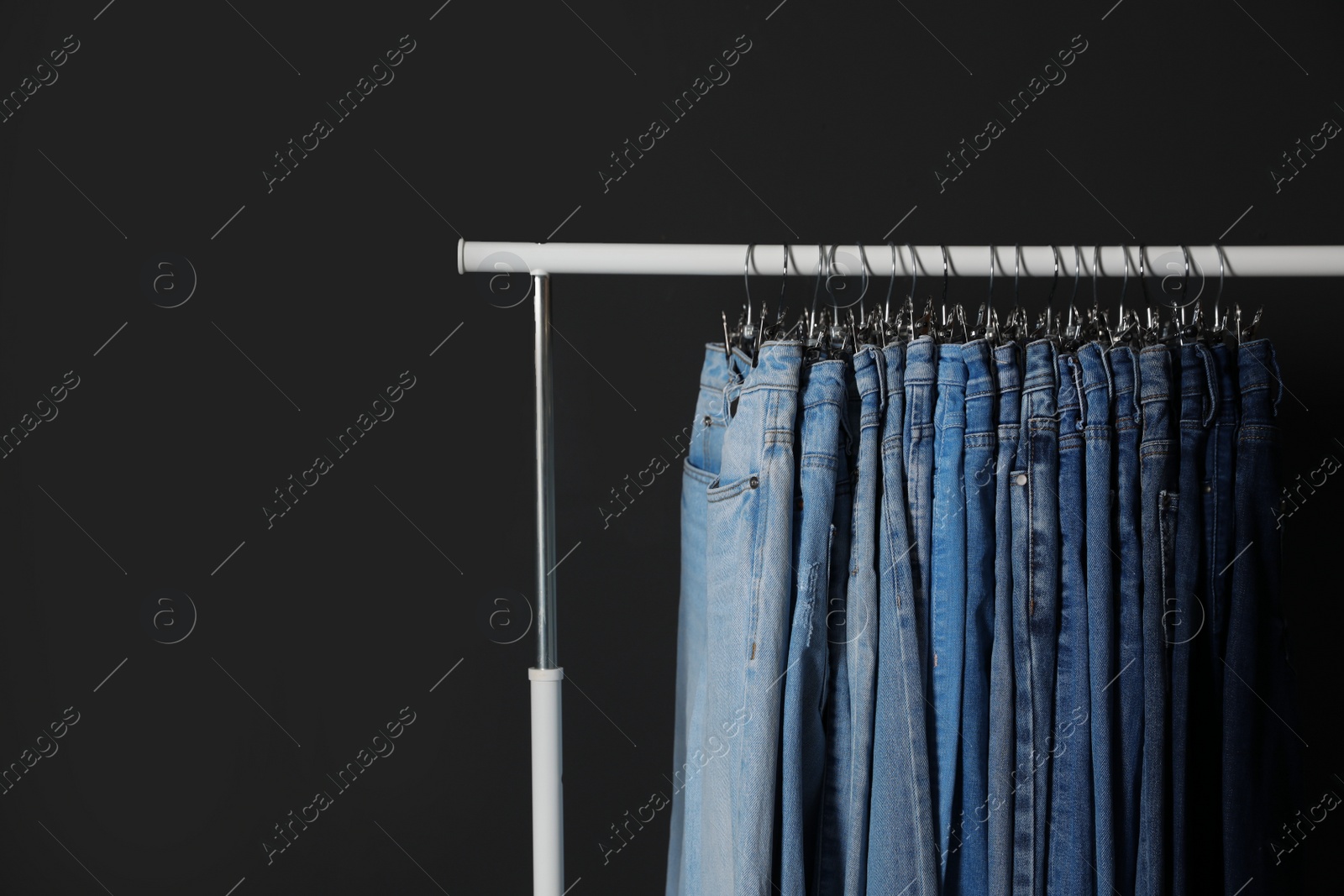 Photo of Rack with different jeans on dark grey background