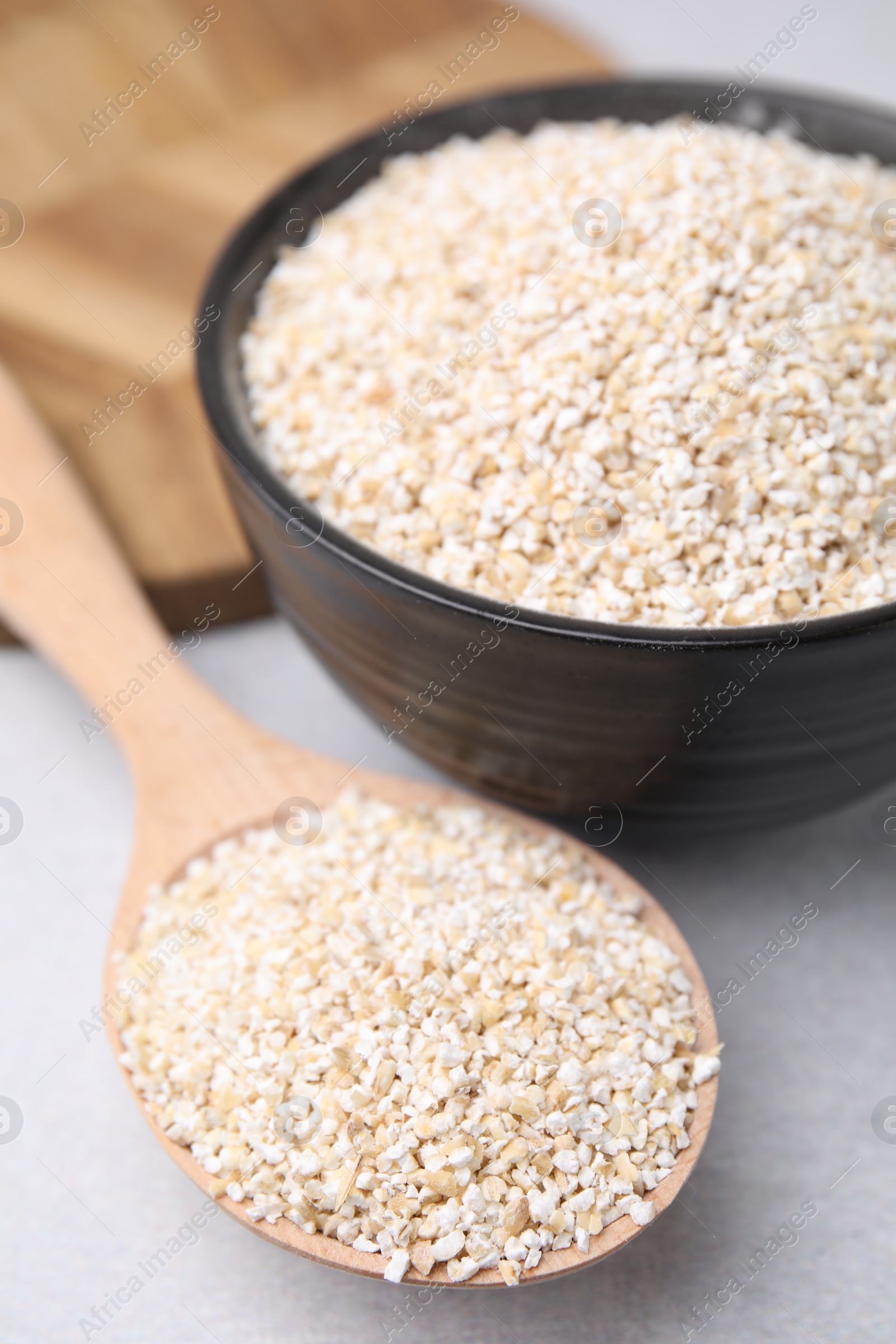 Photo of Dry barley groats in bowl and spoon on light grey table, closeup