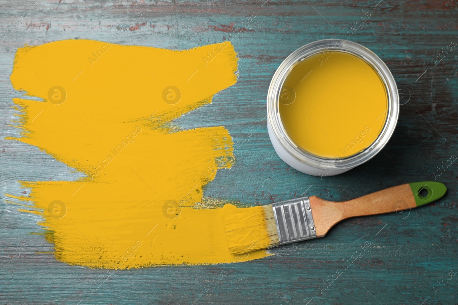 Photo of Can of yellow paint and brush on teal wooden background, flat lay. Space for text