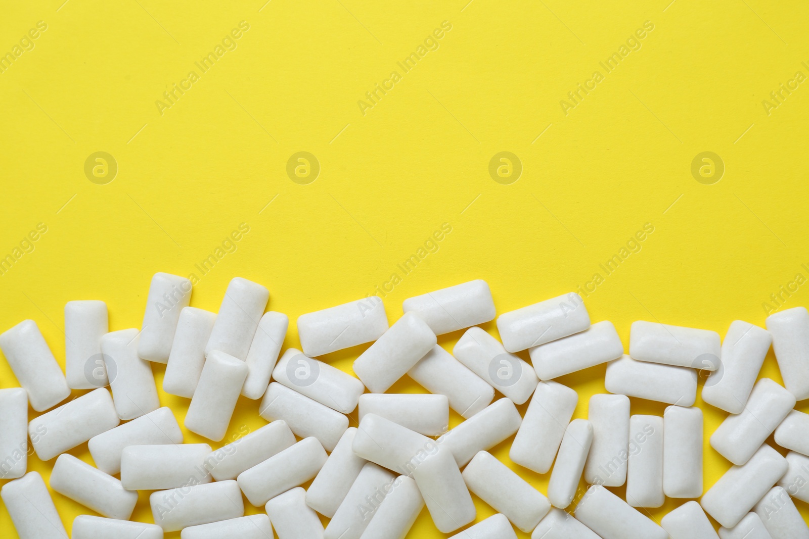 Photo of Tasty white chewing gums on yellow background, flat lay. Space for text