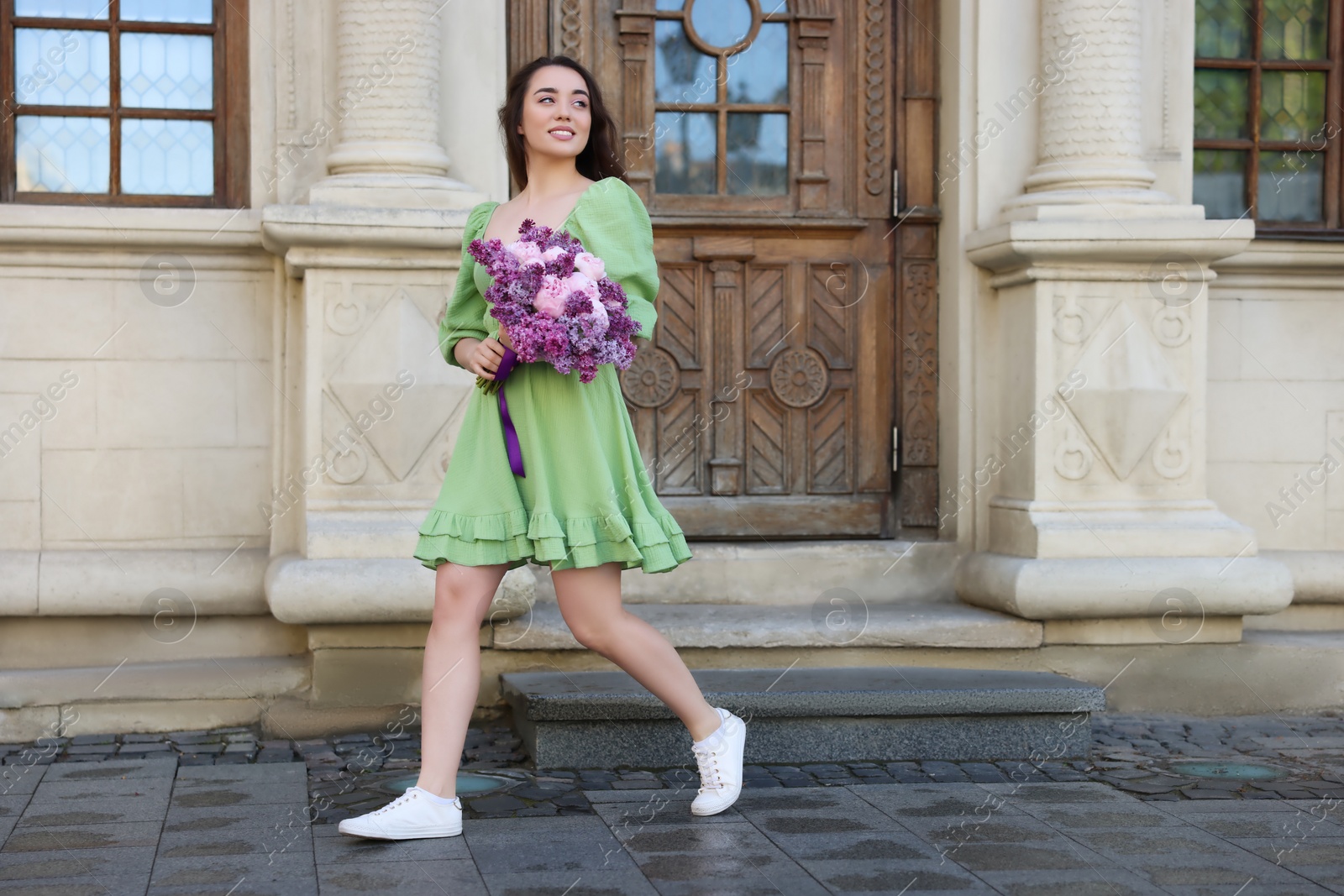 Photo of Beautiful woman with bouquet of spring flowers near building outdoors