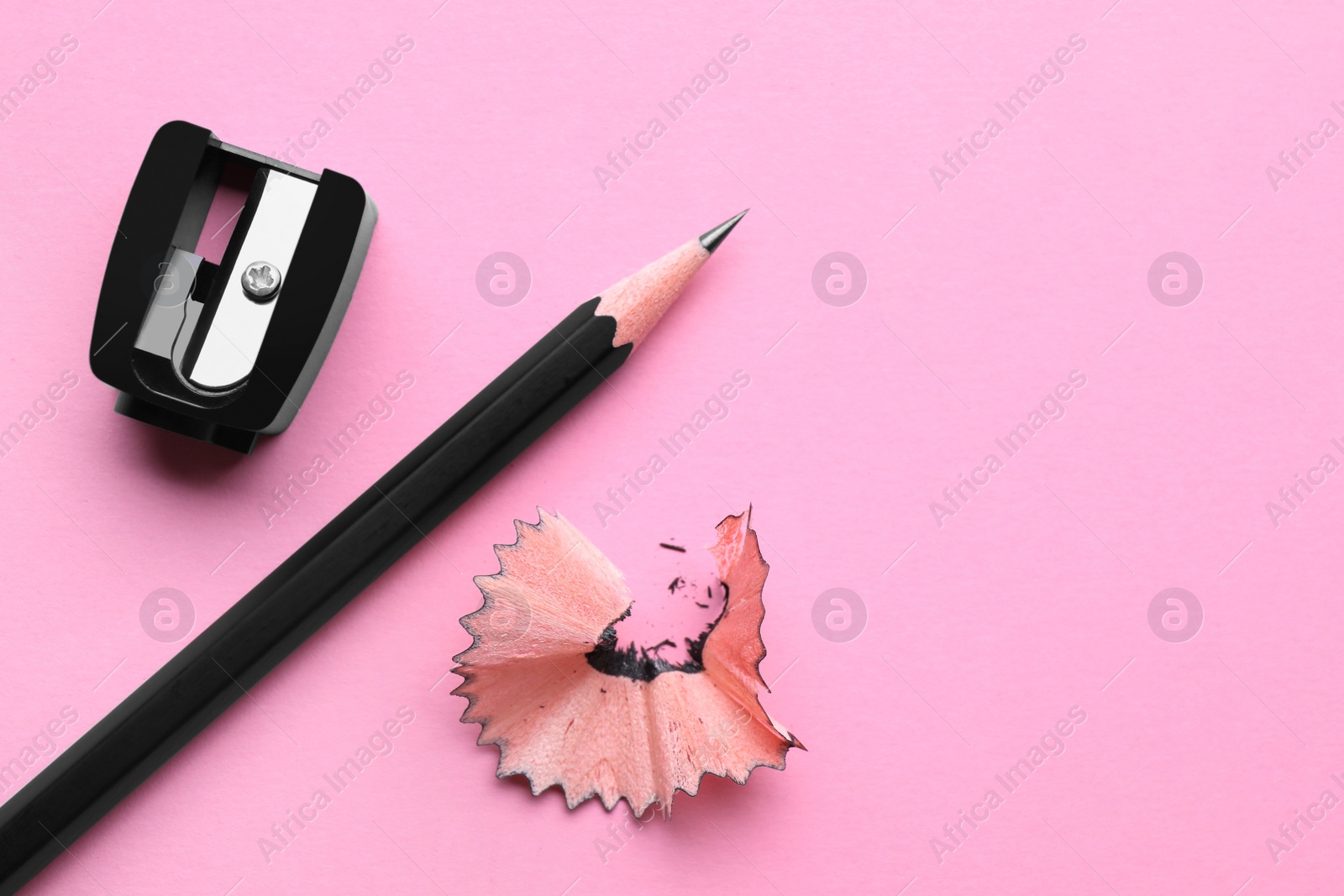 Photo of Pencil, sharpener and shavings on pale pink background, flat lay. Space for text