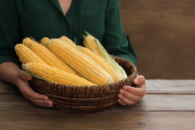 Photo of Woman with bunch of corn cobs at wooden table, closeup