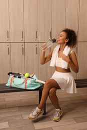 Photo of Beautiful young African American woman drinking water in locker room