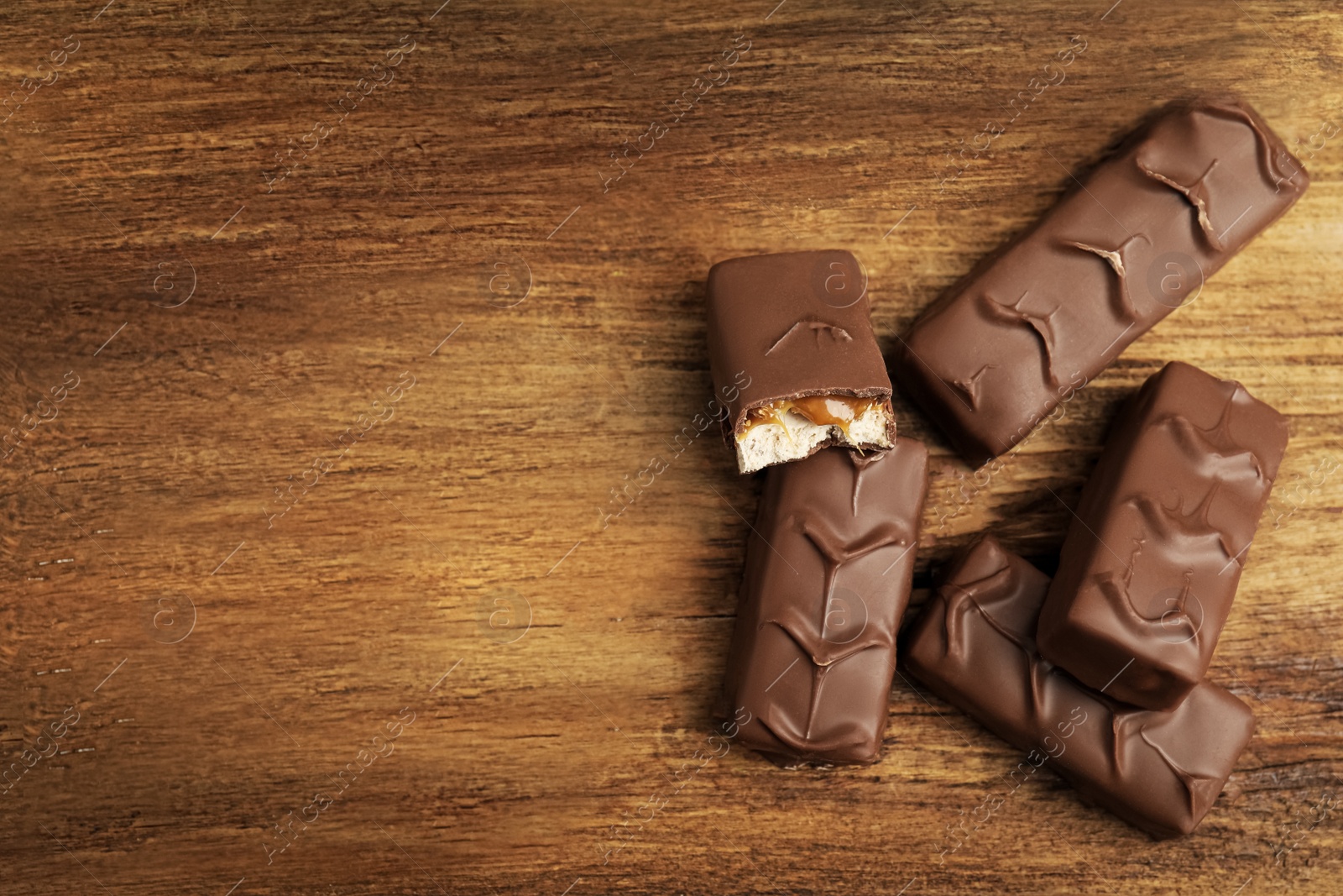 Photo of Chocolate bars with caramel, nuts and nougat on wooden table, flat lay. Space for text