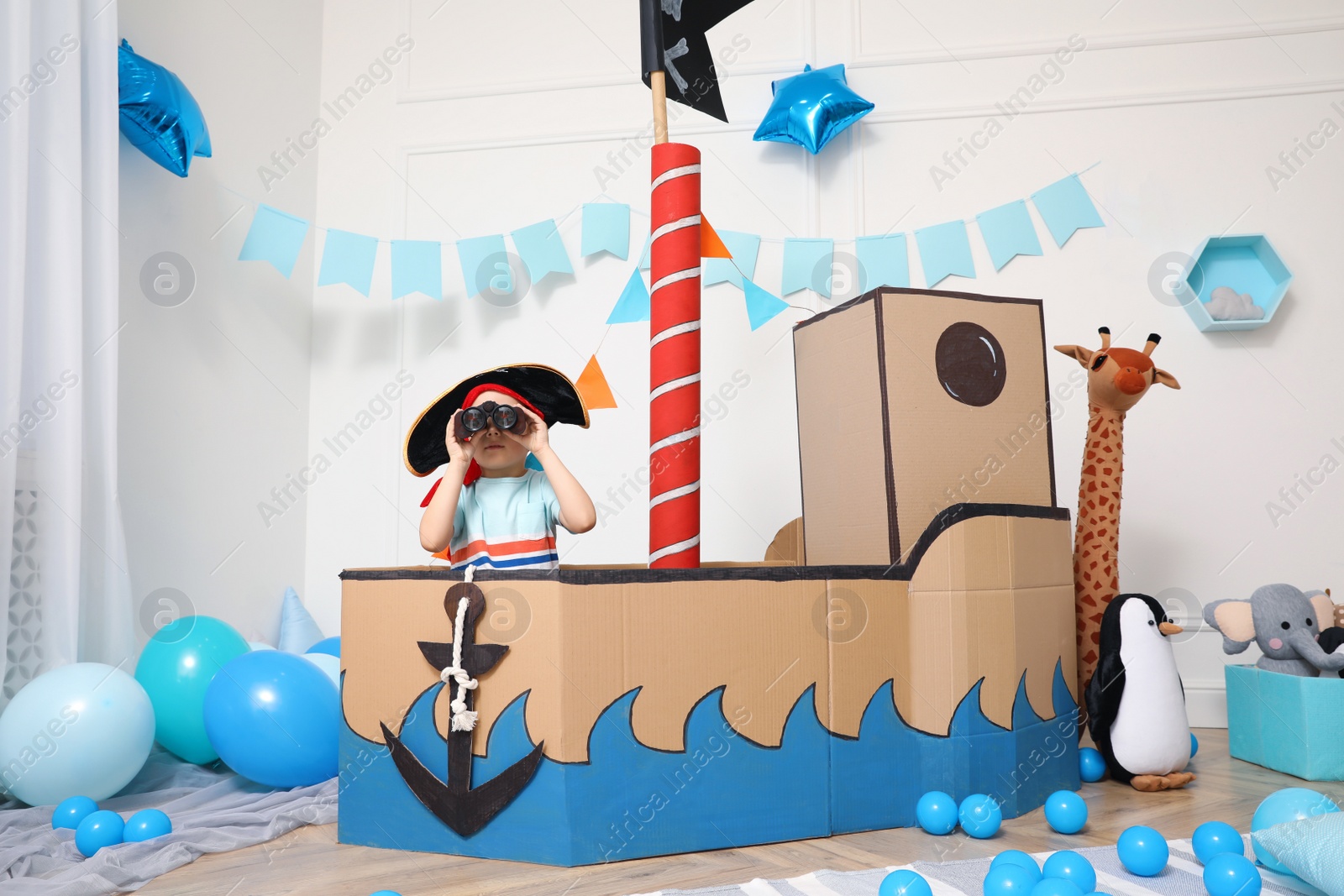 Photo of Little boy playing with binoculars in pirate cardboard ship at home. Child's room interior