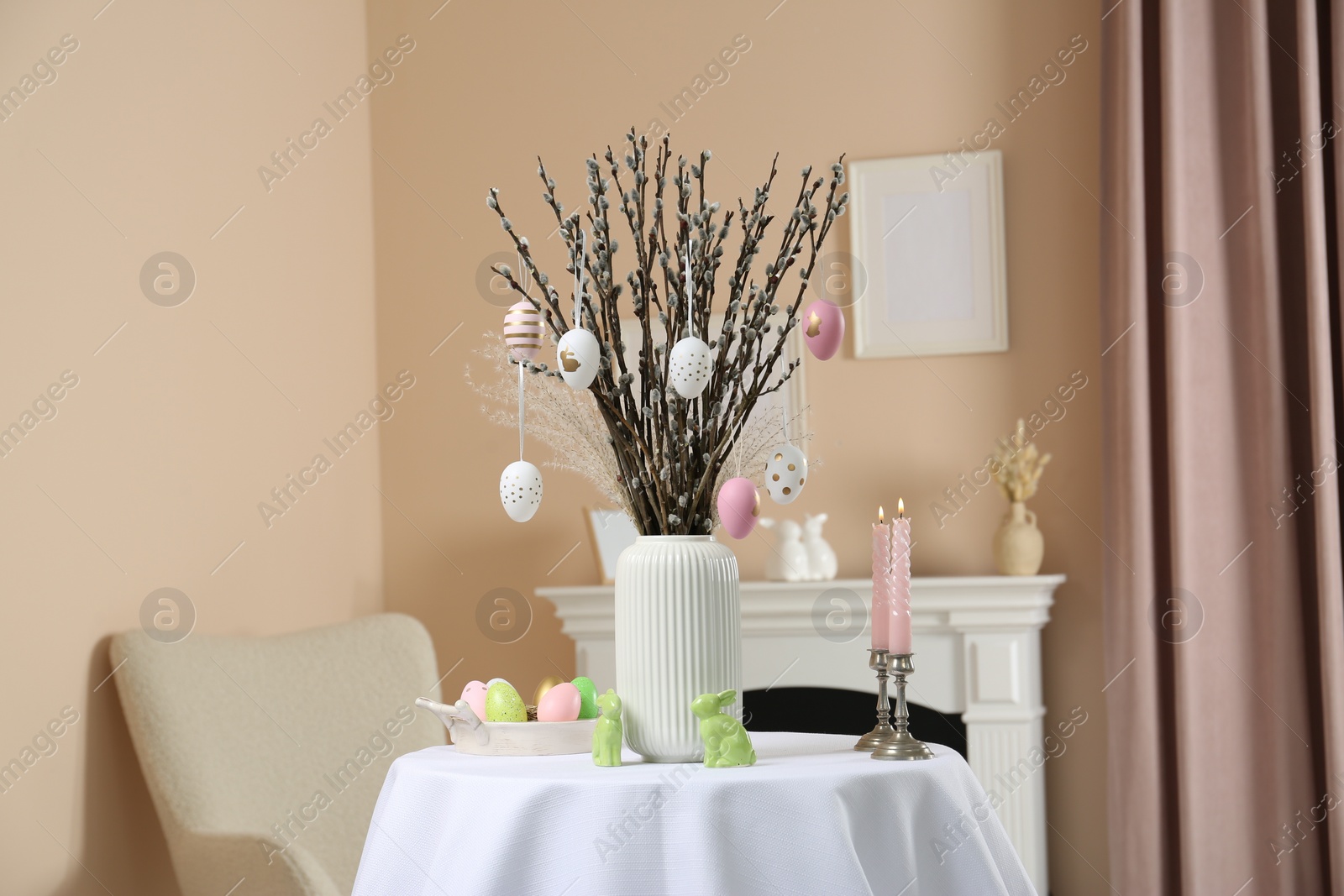 Photo of Pussy willow branches with festively decorated eggs, Easter bunnies and candles on table indoors