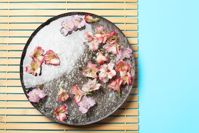 Photo of Bowl of water with flowers on light blue background, top view and space for text. Spa treatment