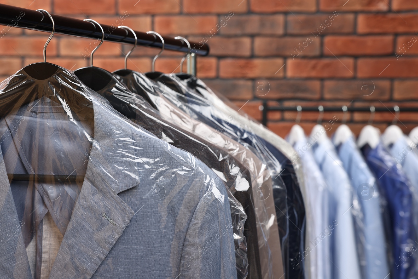 Photo of Dry-cleaning service. Many different clothes hanging on rack against brick wall, closeup