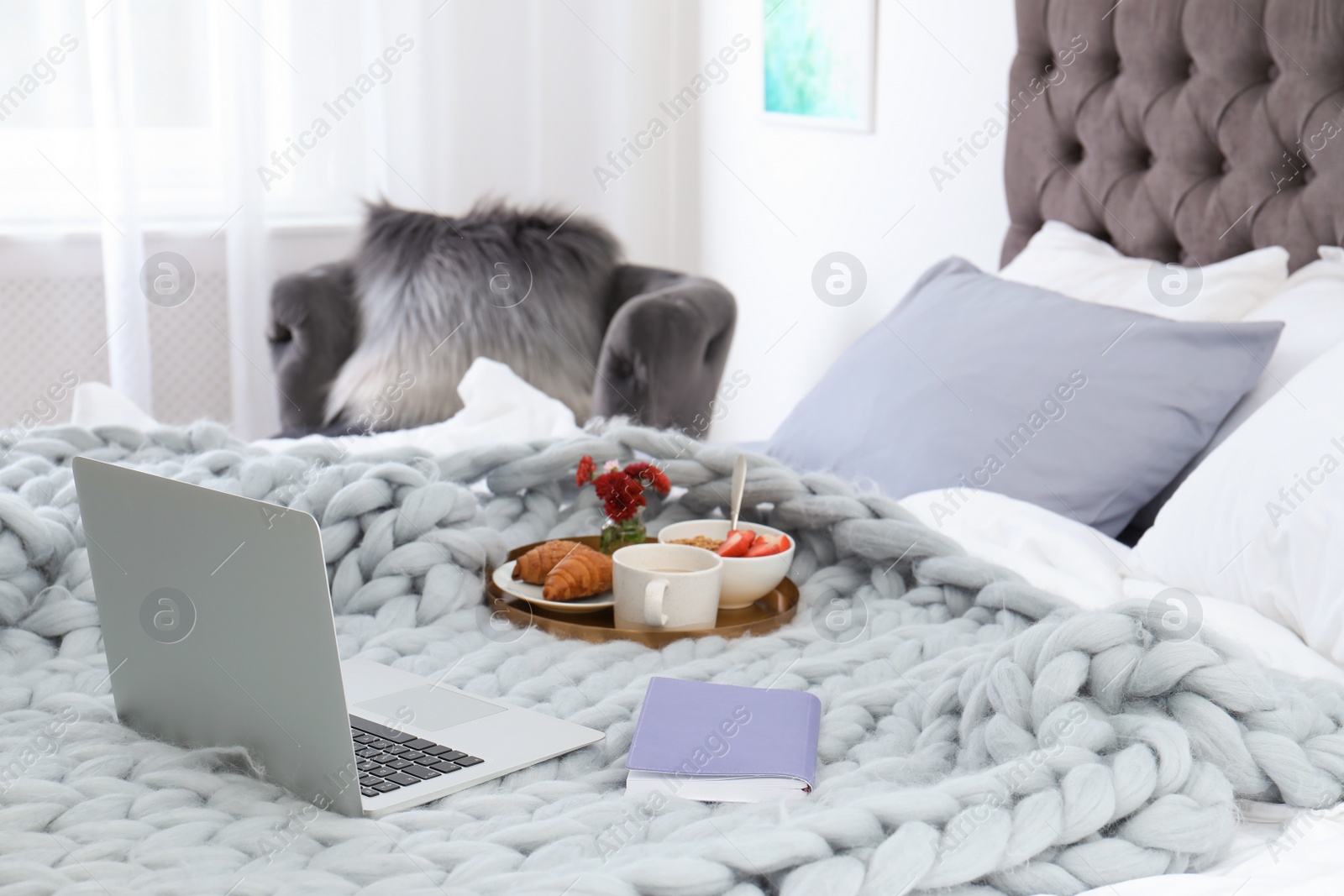 Photo of Laptop, notebook and tray with breakfast on bed in stylish room interior